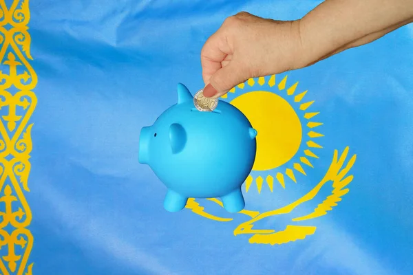 カザフスタンの旗の背景に貯金箱に硬貨を入れる高齢女性の手 手は貯金箱にコインを入れる 退職金だ カザフスタンにおけるお金と退職金の節約 — ストック写真