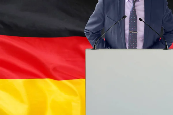 在德国国旗背景上有话筒和穿着西服的男人的论坛报 商人和部落在德国国旗背景上 领奖台上的政治家 手持麦克风背景的德国国旗 — 图库照片