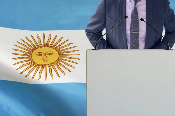 アルゼンチンの国旗を背景にマイクと男とのトリビューン アルゼンチンの国旗を背景にしたビジネスマンと部族 マイクを背景にした表彰台の政治家アルゼンチンの旗 — ストック写真