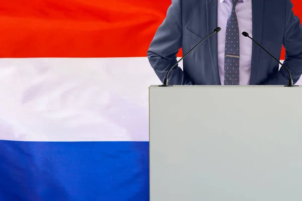 オランダの国旗を背景にマイクと男とのトリビューン ビジネスマンとオランダの旗の背景にトライブリーン マイクを背景にした表彰台の政治家オランダの旗 — ストック写真