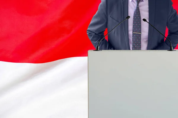 インドネシアの国旗を背景にマイクと男とのトリビューン インドネシアのビジネスマンとトライブリーンが背景にフラグを立てます マイクを背景にした表彰台の政治家インドネシアの旗 — ストック写真