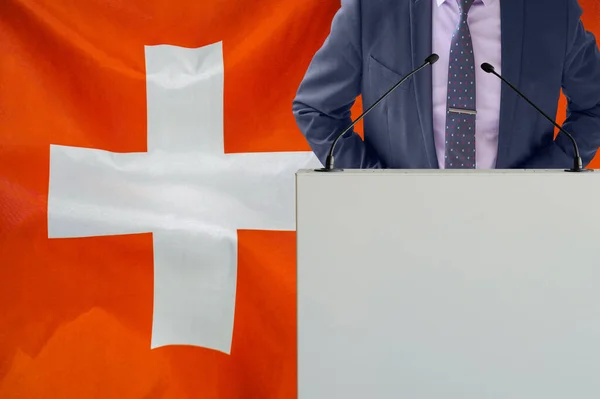 スイスの国旗を背景にマイクと男とのトリビューン ビジネスマンとスイスの旗の背景にトライブリーン マイクを背景にした表彰台の政治家スイスの旗 — ストック写真