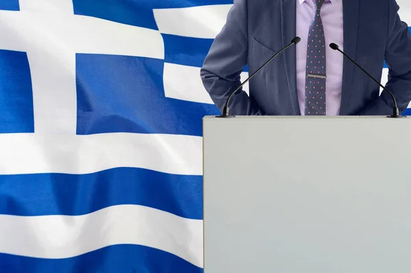 在希腊国旗背景上有话筒和穿着西服的男人的论坛报 商人和部落关于希腊国旗背景的文章 领奖台上的政客 手持麦克风背景的希腊国旗 — 图库照片