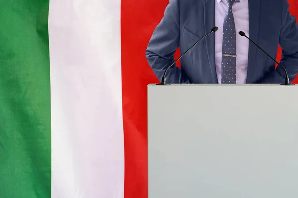 イタリアの国旗を背景にマイクと男とのトリビューン ビジネスマンとイタリアの旗の背景にトライブリーン マイクを背景にした表彰台の政治家イタリアの旗 ビジネス会議 — ストック写真