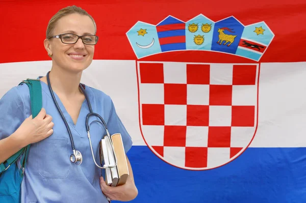 stock image A student doctor in glasses and with a stethoscope and books in her hands looks at the camera against flag of Croatia background. Medical education concept. Medical education in Republic of Croatia