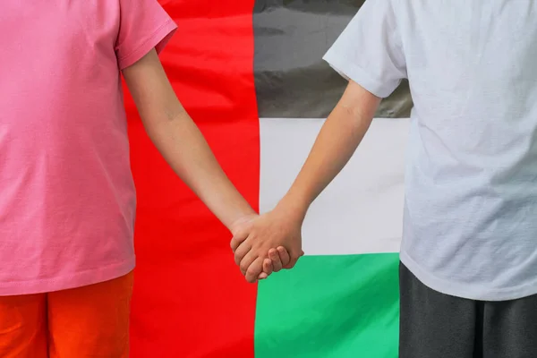 Two children joined hands on flag of United Arab Emirates background. Boy and girl joined hands on flag of United Arab Emirates background. Concept of family and parenting in United Arab Emirates