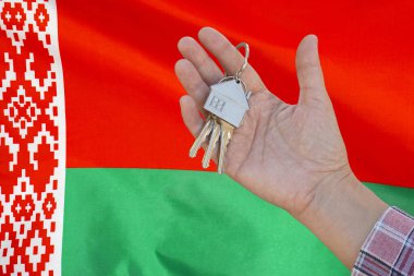 El, Belarus bayrağının arkasındaki dairenin anahtarlarını gösteriyor. Beyaz Rusya bayrağının arka planında bir kadının elinde dairenin anahtarları var. Emlak konsepti ve ev alımı ya da Belarus 'ta yeni bir daire