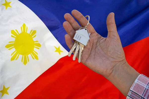 Hand shows the keys to the apartment on background of flag Philippines. Keys to the apartment in a female hand on background of flag Philippines. Realty concept and home buying in Philippines