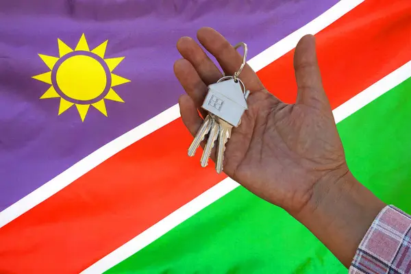Hand shows the keys to the apartment on background of flag Namibia. Keys to the apartment in a female hand on background of flag Namibia. Realty concept and home buying or new apartment in Namibia