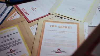Çok gizli belgeler için farklı güvenlik erişim yetkisi etiketleri olan Manila dosyaları. Hassas bilgiler içeren çeşitli renk kodlu zarflar. Modern kapak uyarıları. Ele geçirilen ya da ifşa edilen belgeler