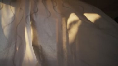 Pencere perdesi ya da kör rüzgarda esiyor güneş içinden geçerken. Evde ya da dairede pencere perdeleri yavaş hareket ediyor. Rüzgarlı havayla güneşli bir gün dalgalı kumaşı hareket ettirir