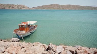 Yunanistan 'ın Girit adasındaki bir kayaya tek bir balıkçı teknesi gelgiti. Yunanistan 'daki huzurlu turkuaz renkli deniz suyunda sessizce hareket eden küçük bir tekne. Arka planda Spinalonga Adası