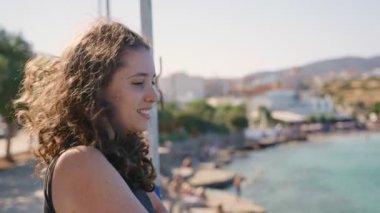 Yazın küçük Yunan plajı ve marina limanı manzarasına bakan genç bir kadın. Rüzgar ve rüzgar, Girit adasında tatil sırasında tipik romantik manzaraya bakan kadın turistlerin saçlarını uçuruyor.