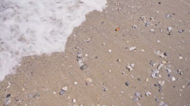 Deniz suyunun yukarıdaki görüntüsü kayaların ve kumların üzerinden kıyıya akıyor. Okyanus ya da gölden gelen tuzlu ya da tatlı su kumlu sahili yıkar. Dalganın berrak suyu