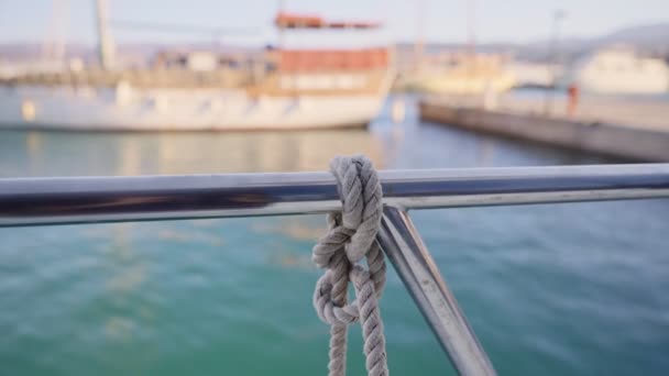 マリーナでドッキングや係留のための厚いナイロン海洋ロープノットで閉じます ボートが午後または港で早朝に背景に浮かんでいるロープでそれに接続されているヨットハンドルバー — ストック動画