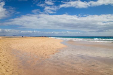 People walk on the wide fine flat sandy beach of Jandia in the south of Fuerteventura, Canary Islands, Spain
