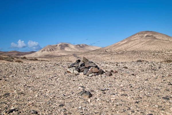 Cairn marker and landscape in the interior of the Canary Island Fuerteventura with the typical volcano cones and the sandy ground in the background