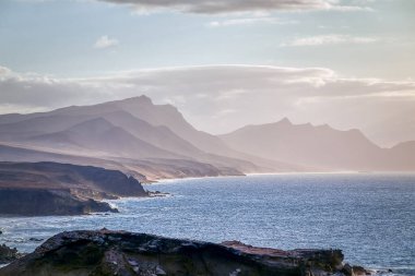 İspanya 'nın Kanarya Adaları' ndaki La Pared köyünden görülen tipik sisli dağlarla Fuerteventura 'nın kayalık batı kıyısı.