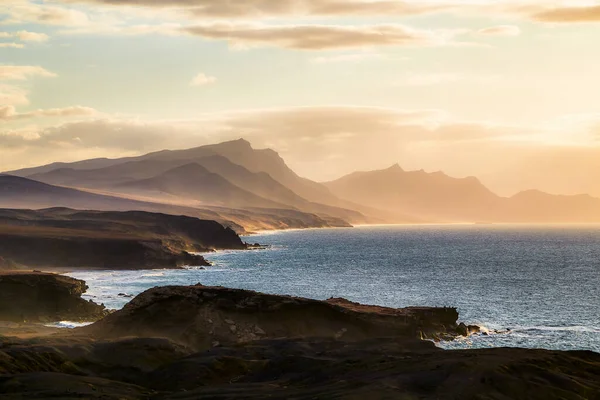 The rocky and indented west coast of Fuerteventura with the typical mountains in the evening light and light veil clouds as seen from the village of La Pared, Canary Islands, Spain