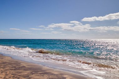 Fuerteventura 'daki kumsal sahili, turkuaz mavi su ve kıyıya vuran hafif dalgalarla.