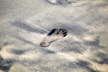 Siyah bej rengi kumdaki tek ayak izi, sağ ayak, sağ üst tarafı işaret ediyor.