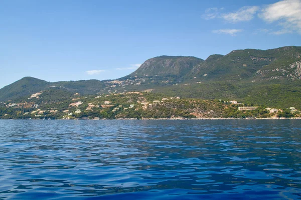 stock image Coastline east coast of Corfu from the sea with green forests on mountain slopes, blue water and buildings by the sea