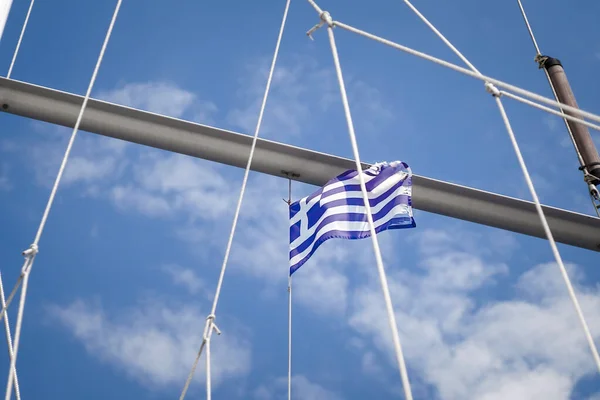 Greek flag waving blue and white in the wind on the masts of a sailing boat against a clear blue sky, it has already been somewhat destroyed by the rough sea wind