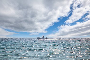 Açık denizde motorlu sandal ve güzel mavi gökyüzü ve hafif bulutlar üzerinde bir adam.