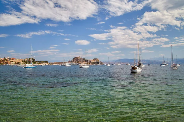 Corfu 'nun eski Kerkyra limanı. Mavi sularda yelkenli tekneleri ve eski kalesi olan.