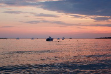 Küçük motorlu tekneler, Corfu 'nun batı kıyısında, kırmızı mavi günbatımında demir atarlar.
