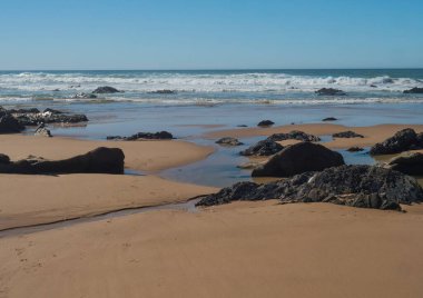 Portekiz, Vila Nova de Milfontes yakınlarındaki Rota Vicentina sahilinde okyanus dalgaları ve keskin kayalarla boş Praia do Queimado plajı manzarası.