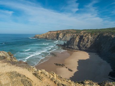 Okyanus dalgaları, uçurumlar ve taşlarla dolu boş Praia das Bernosas plajı, vahşi Rota Vicentina sahillerinde ıslak altın kum ve yeşil bitki örtüsü, Odemira, Portekiz