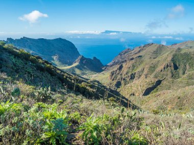 Dramatic lush green picturesque valley. Landscape with sharp rock formation, hills and cliffs seen from hiking trail at Park rural de teno, Tenerife, Canary Islands, Spain. sunny winter day, blue sky.