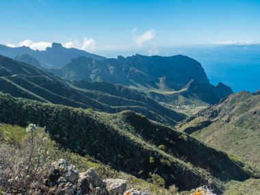 Dramatic lush green picturesque valley. Landscape with sharp rock formation, hills and cliffs seen from hiking trail at Park rural de teno, Tenerife, Canary Islands, Spain. sunny winter day, blue sky.