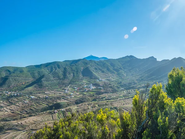 Lush green valley with terraced fields and village Las Portelas. Landscape with rocks and hills seen from hiking trail at Park rural de Teno, Tenerife, Canary Islands, Spain. sunny day, blue sky.