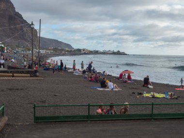 Valle Gran Rey, La Gomera, Kanarya Adaları, 26 Aralık 2021: Yerel halk ve turistler La Playa köyündeki Playa de La Calera volkanik kumsalında dinleniyorlar. Bulutlu kış günü.