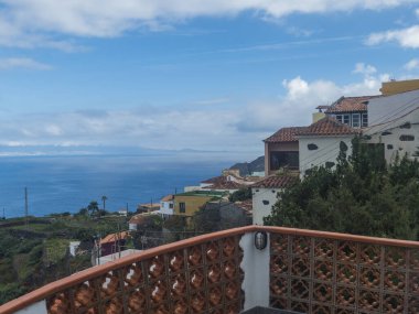 Kuzey kıyısındaki yeşil vadide renkli geleneksel evleri, tarlaları ve okyanusu olan eski Agulo köyü manzarası. Bulutlu bir kış günü. La Gomera, Kanarya Adaları, İspanya.