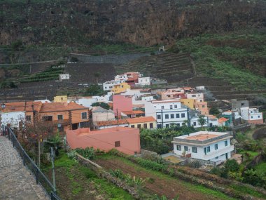 Renkli geleneksel evleri, tarlaları ve kuzey kıyısındaki yeşil vadideki dağları olan eski Agulo köyü manzarası. Bulutlu bir kış günü. La Gomera, Kanarya Adaları, İspanya.