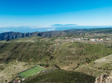 Fortaleza Dağı 'nın zirvesinden görülen Chipude köyündeki hava manzarası. Beyaz bulutlar ve La Palma adası yukarıda, mavi gökyüzü. La Gomera, Kanarya Adaları, İspanya