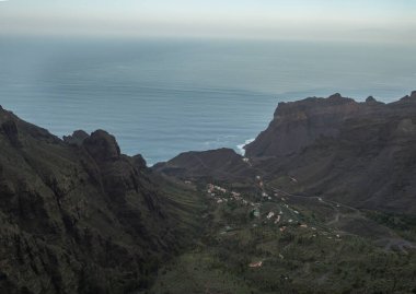 Küçük evleri, keskin uçurumları ve Atlantik okyanusu olan Taguluche köyüne bakan hava manzaralı Mirador Ermita del Santo, Arure. La Gomera, Kanarya Adaları, İspanya.