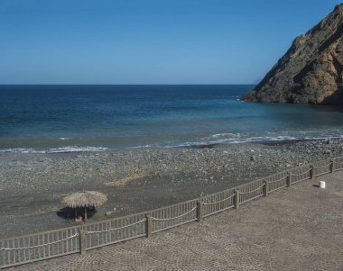 Playa de Vallehermoso manzarası, volkanik siyah kumlu kumsal çakıl taşları ve güneş şemsiyeli koy mavi okyanus ve gökyüzü. Vallehermoso, La Gomera, Kanarya Adaları, İspanya.