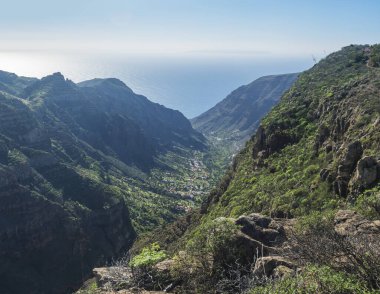 Sabah erken saatlerde Arure köyünün yeşil vadisindeki palmiye ağaçları ve geleneksel renkli evleri. Valle Gran Rey, La Gomera, Kanarya Adaları, İspanya, Avrupa. Mavi gökyüzü beyaz bulutlar arka plan.