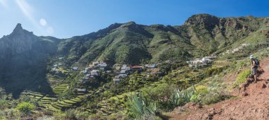 Yürüyüşçü, İmada köyü ile birlikte Barranco de Guarimiar Gorge 'da yürüyüş yaparken manzara seyrediyor. Palmiye ağaçları ve sulu bitkilerle dolu yeşil dağ kanyonu. La Gomera, Kanarya Adaları, İspanya.