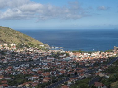 Portekiz 'in Madeira adasının doğu kıyısındaki Machico kasabasının panoramik manzarası, güneşli bir günde liman, sahil, evler ve yeşil tepeler ile popüler bir turizm beldesi.