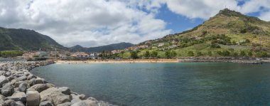 Machico koyunun panoramik manzarası. Altın kumsal, palmiye ağaçları ve yeşil dağlarla çevrili evler. Machico Madeira 'nın doğu kıyısında popüler bir tatil köyüdür..