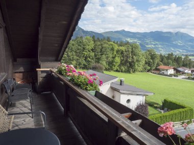 Avusturya 'nın Tyrol kentindeki Alpler ve Achensee Gölü' nün bulunduğu yeşil vadiye doğru Wiesing köyündeki sardunya çiçekleri, masa ve sandalyelerle ahşap balkondan görüntü. Yaz güneşli bir gün..