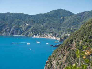 Monterosso al Mare 'nin kumsalı, gemileri ve tekneleri olan, yeşil uçurumlar, kayalar, açık mavi gökyüzü ve deniz ile Azure Trail' den Vernazza 'ya görünen uzak görüntüsü. Ulusal park Cinque Terre, Liguria, İtalya