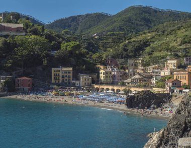 Monterosso al Mare 'nin sahili, renkli evleri, tren rayları, çan kulesi ve yeşil kayalıkları olan Torre Bastioni' nin açık mavi gökyüzü ve deniz manzarası. Ulusal park Cinque Terre, Liguria, İtalya.