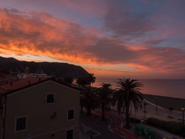 Riva Trigoso plajında güzel turuncu gün batımı. Avuç içleri ve evleri gezinti güvertesinde. Sestri Levante, Liguria, İtalya.