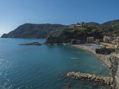 Monterosso al Mare 'nin sahili, renkli evleri, tren rayları, çan kulesi ve yeşil kayalıkları olan Torre Bastioni' nin açık mavi gökyüzü ve deniz manzarası. Ulusal park Cinque Terre, Liguria, İtalya.